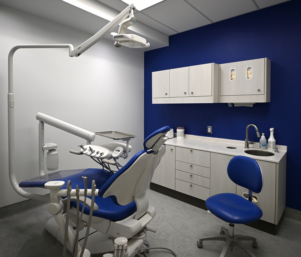 Contemporary dental treatment room with a white and blue color scheme, showcasing ergonomic dental equipment, sleek cabinetry, and a bold blue accent wall for a clean, professional atmosphere.