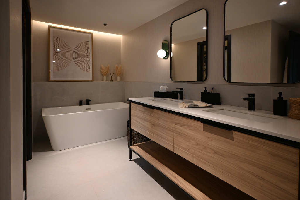 Modern minimalist bathroom with a freestanding white tub, black matte fixtures, a double-sink vanity with wood cabinetry, and ambient lighting highlighting wall art and pampas grass decor.
